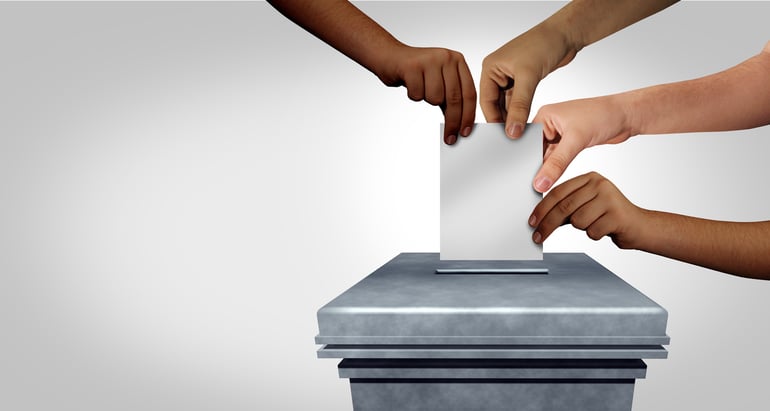 Four hands holding a ballot above a ballot box