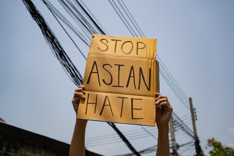 A person holds a sign that reads "STOP ASIAN HATE"