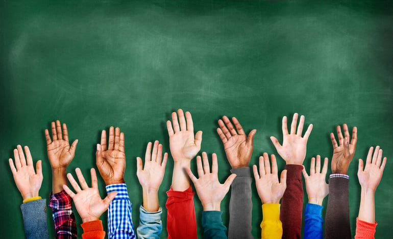 Children's hands raised in front of a chalkboard.